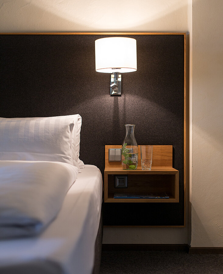 Detailansicht eines Nachttischs mit Lampe und Bett im Hotelzimmer des Hotel-Landgasthof KREUZ