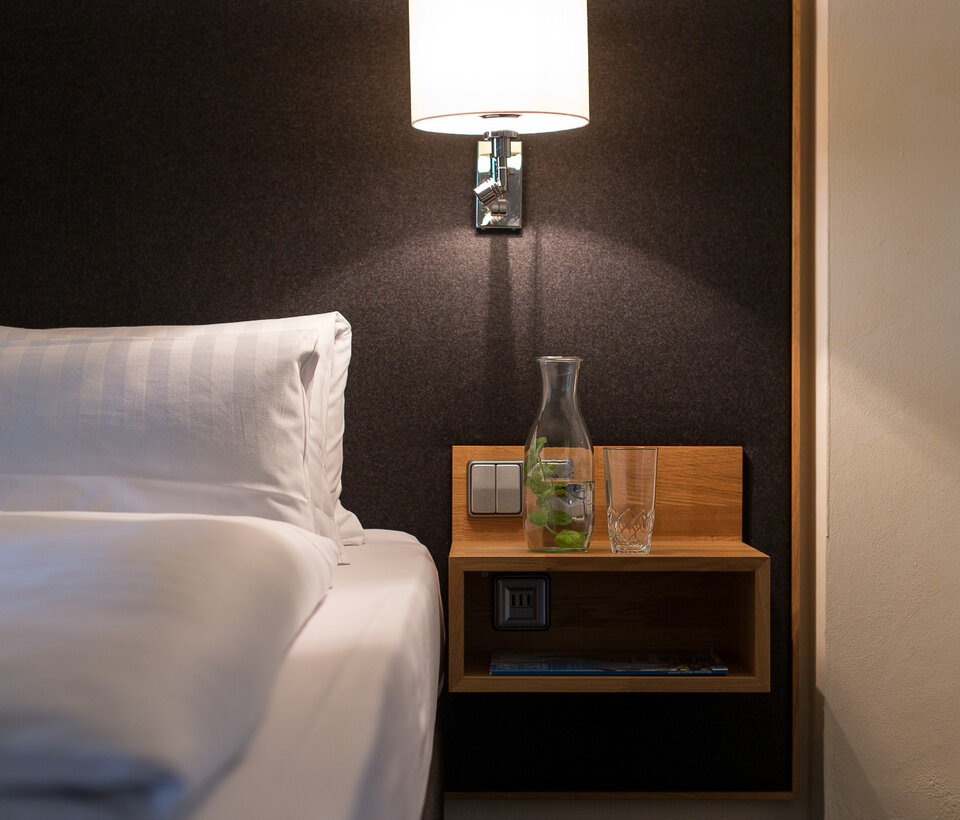 Detailansicht eines Nachttischs mit Lampe und Bett im Hotelzimmer des Hotel-Landgasthof KREUZ