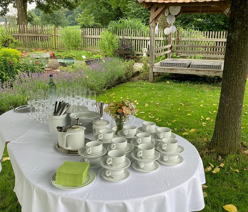 Rund gedeckter Tisch mit weißer Tischdecke im Garten