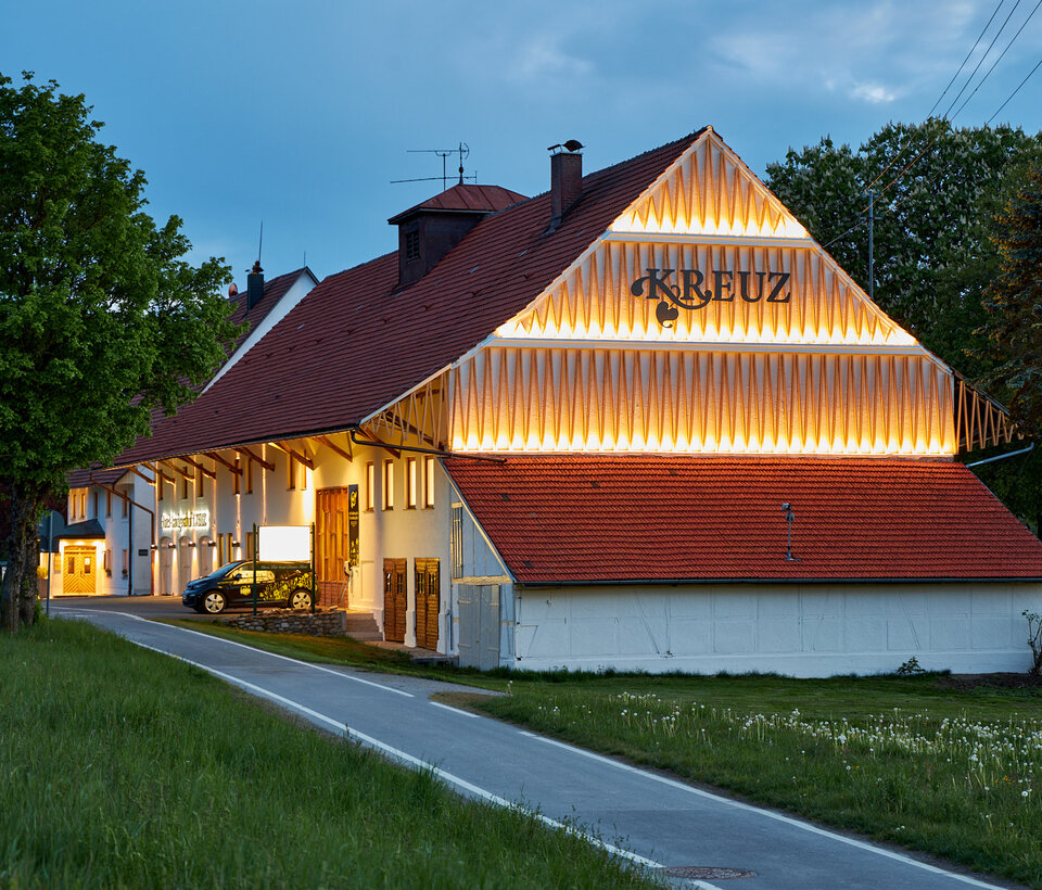 Traditionelles Gebäude des Hotel-Landgasthof KREUZ mit rotem Dach und beleuchteter Fassade bei Dämmerung