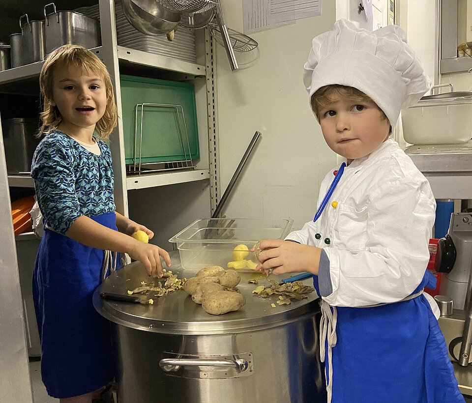 Zwei Kinder gemeinsam an großen Töpfen in der Küche