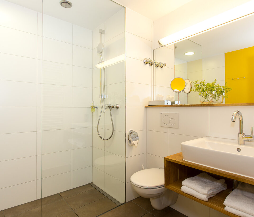 Modernes Bad mit Dusche, gelber Wandgestaltung und Handtüchern im Hotel-Landgasthof KREUZ