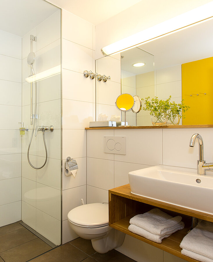 Modernes Bad mit Dusche, gelber Wandgestaltung und Handtüchern im Hotel-Landgasthof KREUZ